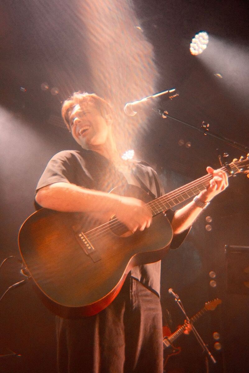 Singer laughing with an acoustic guitar under a spotlight